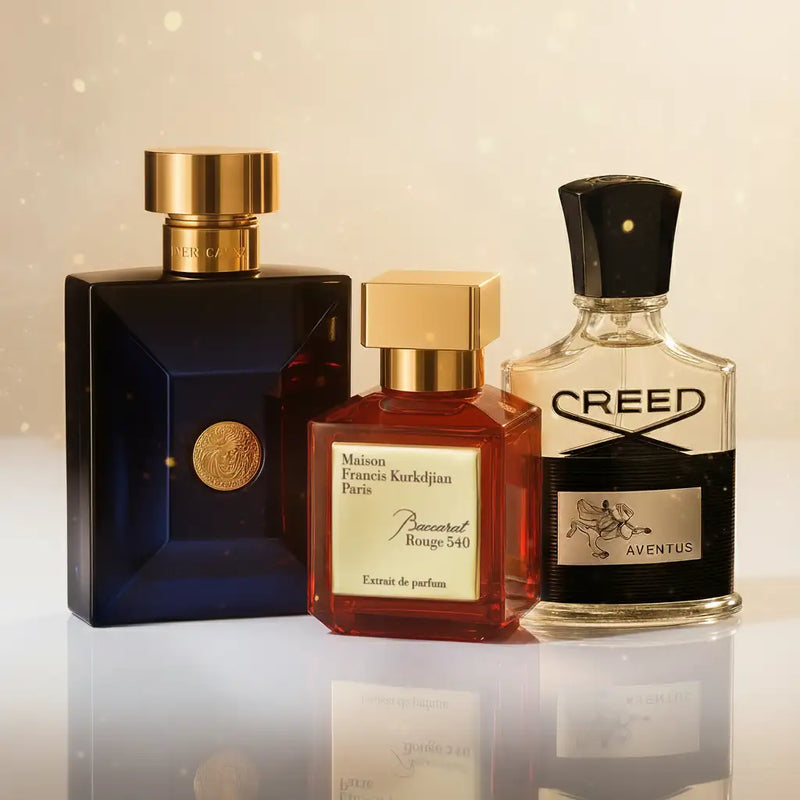 Three luxury perfume bottles, maison francis kurkdjian’s rouge 540 in a faceted amber glass with gold cap, versace’s eros in deep blue crystal with golden medallion and lid, and creed aventus in clear