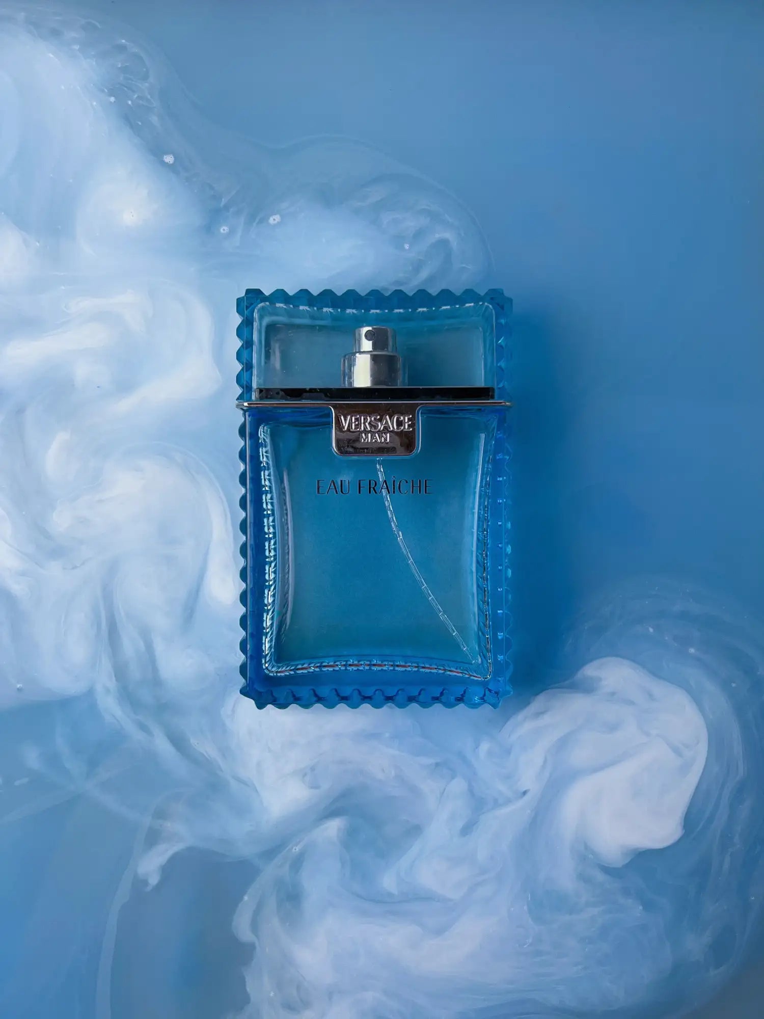 A translucent blue glass bottle with a silver cap and embossed edges, featuring the ’versace man’ label.